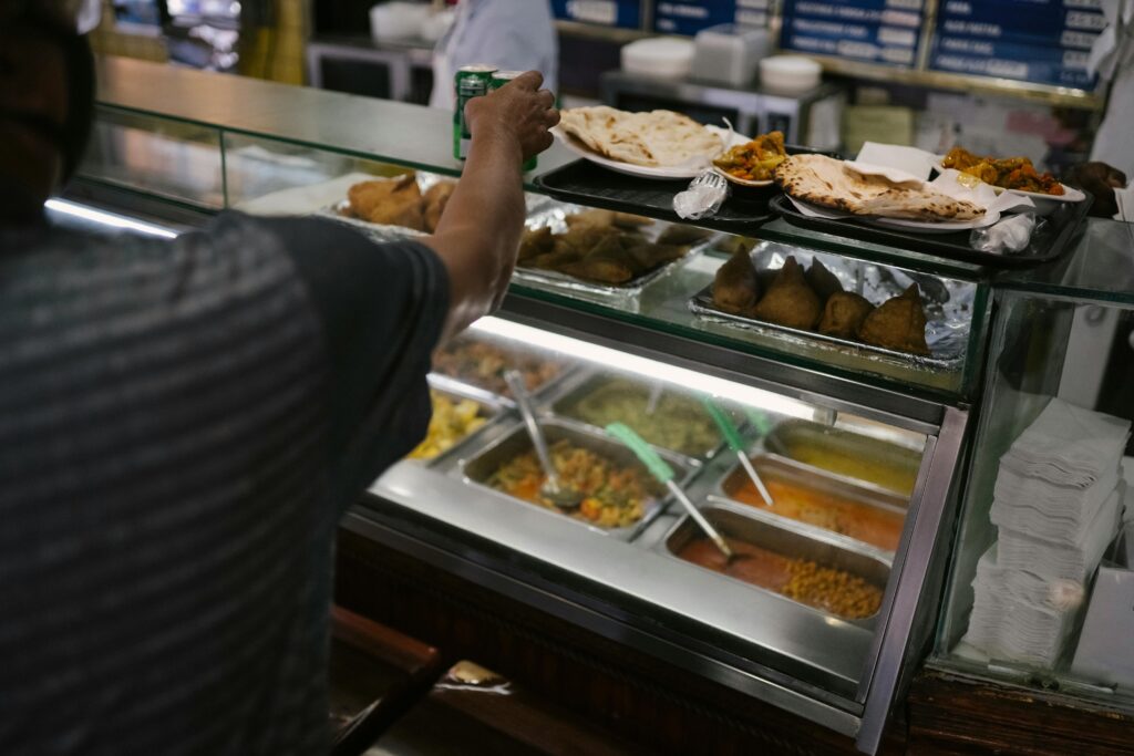 A customer chooses plates of Indian food from a buffet with diverse dishes on display.